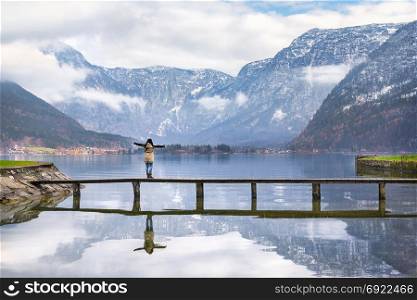Holiday destinations theme image of a woman with open arms enjoying the lovely Hallstatter lake and the peaks of the Dachstein Mountains, in Hallstatt, Austria.