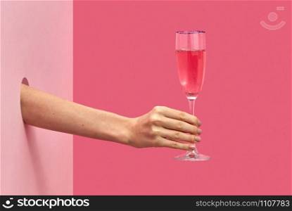 Holiday glass of rose wine in a female&rsquo;s hand through the hole in the wall on a duotone pink background with soft shadows, copy space. Holiday concept.. Woman&rsquo;s hand holds glass of rose wine with soft shadows.