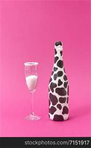 Holiday glass of white powder as a sugar and creative painted bottle with black spots on a hot pink background, copy space. Congratulation card.. Painted black spots wine bottle with glass of white powder.