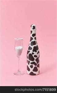 Holiday glass of white powder as a sugar and painted bottle with black spots on a light millennial pink background, copy space. Congratulation card.. Creative painted wine bottle with black spots and glass of white powder.