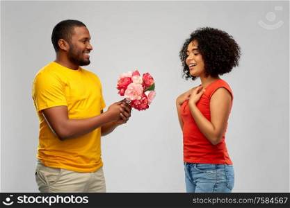 holiday, greeting and people concept - happy african american couple with bunch of flowers over grey background. happy african american couple with flowers