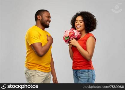 holiday, greeting and people concept - happy african american couple with bunch of flowers over grey background. happy african american couple with flowers