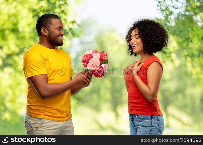 holiday, greeting and people concept - happy african american couple with bunch of flowers over green natural background. happy african american couple with flowers