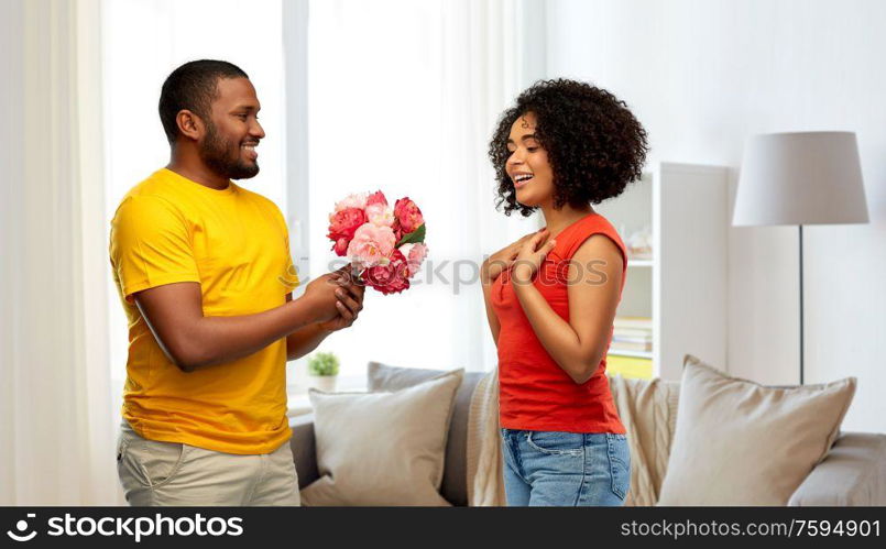 holiday, greeting and people concept - happy african american couple with bunch of flowers over home background. happy african american couple with flowers