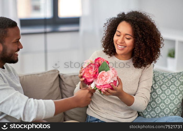 holiday, greeting and people concept - happy african american couple with bunch of flowers at home. happy couple with bunch of flowers at home