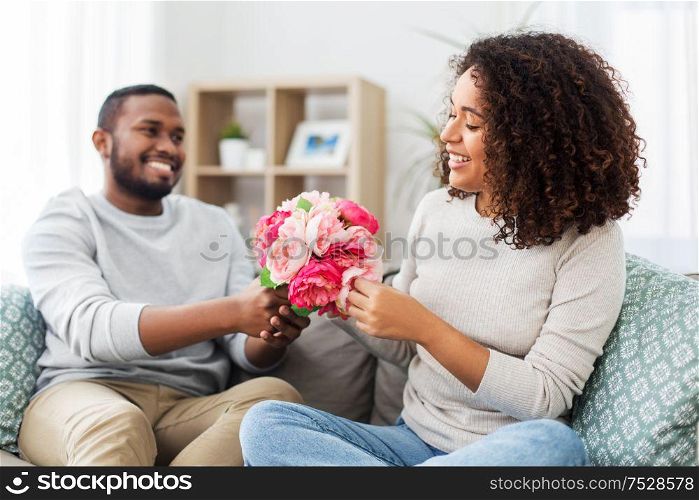 holiday, greeting and people concept - happy african american couple with bunch of flowers at home. happy couple with bunch of flowers at home