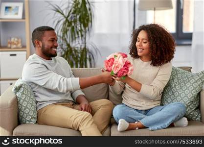 holiday, greeting and people concept - happy african american couple with bunch of flowers at home. happy couple with bunch of flowers at home