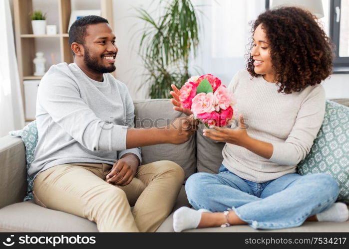 holiday, greeting and people concept - happy african american couple with bunch of flowers at home. happy couple with bunch of flowers at home