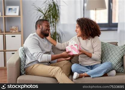 holiday, greeting and people concept - happy african american couple with gift at home. happy couple with gift at home