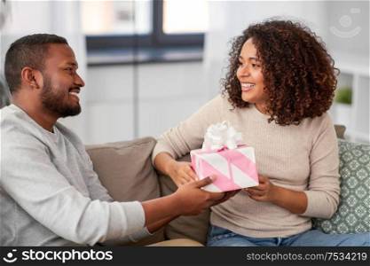 holiday, greeting and people concept - happy african american couple with gift at home. happy couple with gift at home