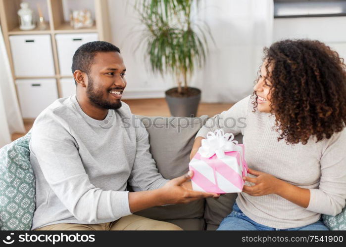 holiday, greeting and people concept - happy african american couple with gift at home. happy couple with gift at home