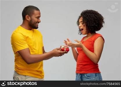 holiday, greeting and people concept - happy african american couple with small red gift box over grey background. happy african american couple with red gift box