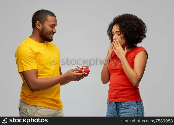 holiday, greeting and people concept - happy african american couple with small red gift box over grey background. happy african american couple with red gift box