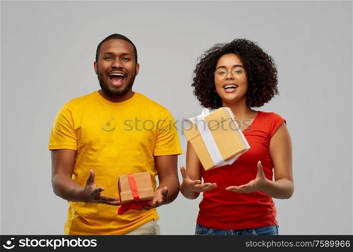 holiday, greeting and people concept - happy smiling african american couple throwing gift boxes over grey background. happy african american couple throwing gift boxes