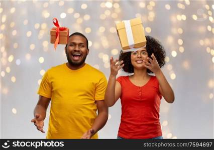 holiday, greeting and people concept - happy smiling african american couple throwing gift boxes over festive lights background. happy african american couple throwing gift boxes