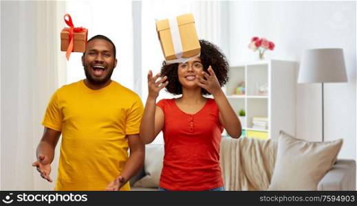 holiday, greeting and people concept - happy smiling african american couple throwing gift boxes over home background. happy african american couple throwing gift boxes