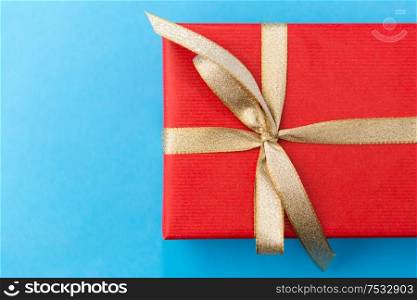 holiday, greeting and surprise concept - christmas red gift box with golden bow on blue background. christmas red gift box on blue background