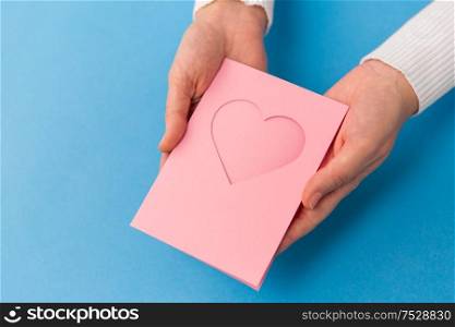 holiday, love and valentines day concept - close up of hands holding greeting card with heart on blue background. hands holding greeting card with heart