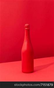 Holiday mock up bottle of champagne red painted spray on a duotone red background with soft shadows, copy space. Minimal concept.. Red painted spray wine bottle on a duotone red background.