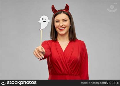 holiday, photo booth and people concept - happy smiling woman in red halloween costume of devil with horns and ghost party accessory over grey background. happy woman in red halloween costume of devil