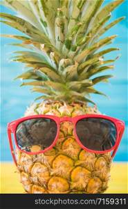 Holiday pineapple have sunglasses on blue wooden background, tropical holiday concept