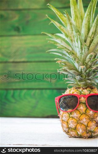 Holiday pineapple have sunglasses on green wooden background, tropical holiday concept