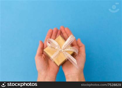 holiday, presents and greetings concept - hands holding small christmas gift box on blue background. hands holding small christmas gift box