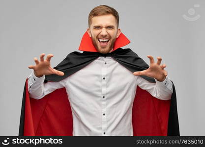 holiday, theme party and people concept - man in halloween costume of vampire and dracula cape scaring over grey background. man in halloween costume of vampire scaring