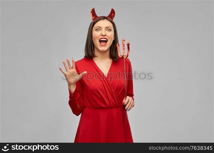holiday, theme party and people concept - scary woman in red halloween costume of devil with horns and trident over grey background. scary woman in red halloween costume of devil