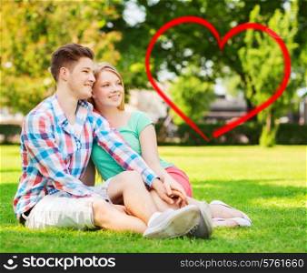 holiday, valentine&#39;s day, dating and love concept - happy couple sitting on grass in summer park with red heart shape