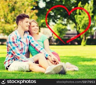 holiday, valentine&amp;#39;s day, dating and love concept - happy couple sitting on grass in summer park with red heart shape
