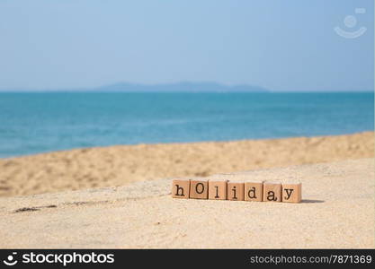 Holiday word on wood rubber stamps stack on the sand beach for vacation and summer season concept, beautiful sea view during daytime on a sunny day with blue sky on background