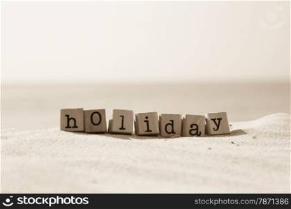 Holiday word on wood rubber stamps stack on the sand beach for break and vacation concept, ocean view on background, sepia tone image