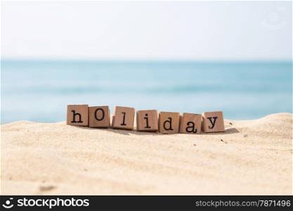 Holiday word on wood rubber stamps stack on the sand beach for vacation and summer season concept, beautiful ocean view during daytime on a sunny day with blue sky on background