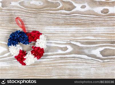 Holiday wreath, heart shaped, in USA national colors on rustic white wooden boards. Fourth of July holiday concept for United States of America.