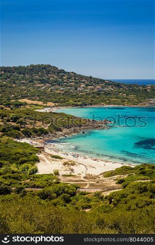 Holidaymakers in the crystal clear turquoise Mediterranean sea at Bodri beach in the Balagne region of Corsica with railway line and maquis in the foreground and deep blue sky