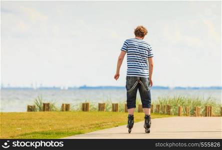 Holidays, active lifestyle freedom concept. Young fit man on roller skates riding outdoors on sea coast, guy rollerblading on sunny day