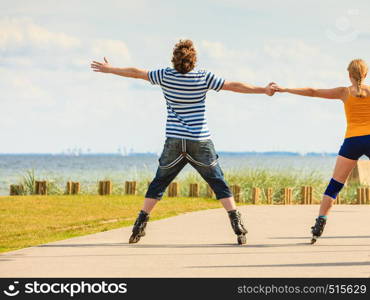 Holidays, active people and friendship concept. Young fit couple on roller skates riding outdoors on sea coast, woman and man rollerblading together on the promenade