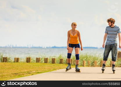 Holidays, active people and friendship concept. Young fit couple on roller skates riding outdoors on sea shore, woman and man rollerblading together on the promenade