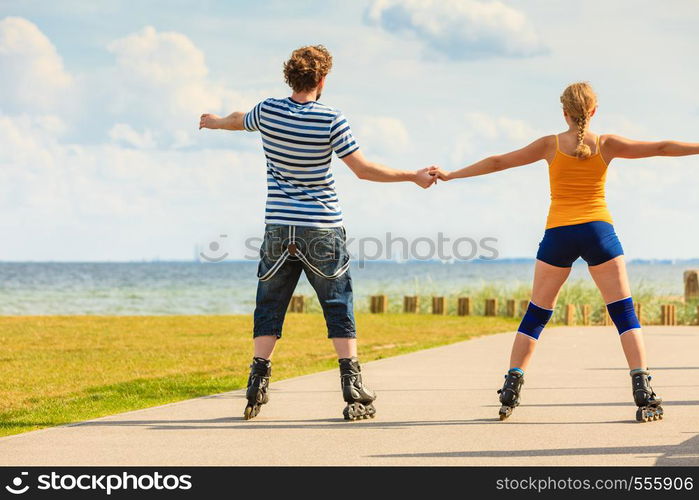 Holidays, active people and friendship concept. Young fit couple on roller skates riding outdoors on sea coast, woman and man rollerblading together on the promenade