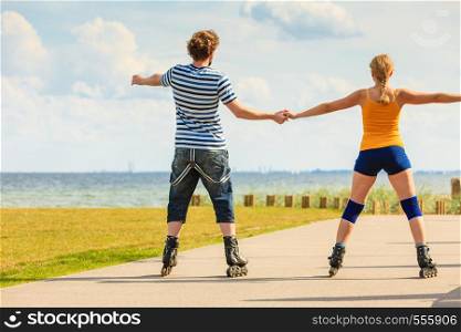 Holidays, active people and friendship concept. Young fit couple on roller skates riding outdoors on sea coast, woman and man rollerblading together on the promenade