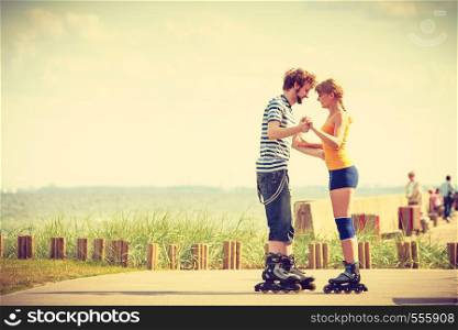 Holidays, active people and friendship concept. Young fit couple on roller skates riding outdoors on sea shore, woman and man rollerblading together on the promenade