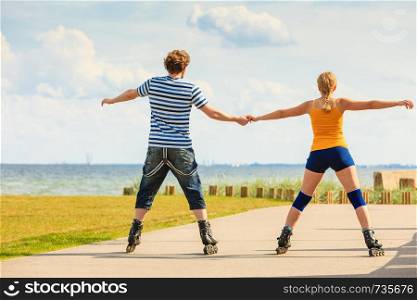 Holidays, active people and friendship concept. Young fit couple on roller skates riding outdoors on sea coast, woman and man rollerblading together on the promenade
