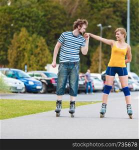 Holidays, active people and friendship concept. Young fit couple on roller skates riding outdoors, woman and man rollerblading together on city street