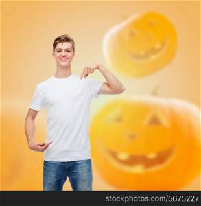 holidays, advertisement and people concept - smiling young man in blank white t-shirt pointing fingers at himself over halloween pumpkins background