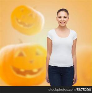 holidays, advertisement and people concept - smiling young woman in blank white t-shirt over halloween pumpkins background