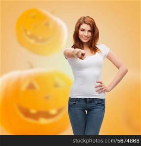holidays, advertisement, gesture and people concept - smiling young woman in blank white t-shirt pointing finger at you over halloween pumpkins background