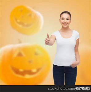 holidays, advertisement, gesture and people concept - smiling young woman in blank white t-shirt showing thumbs up over halloween pumpkins background