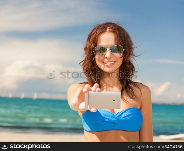 holidays and beach concept - beautiful woman in bikini and sunglasses with smartphone