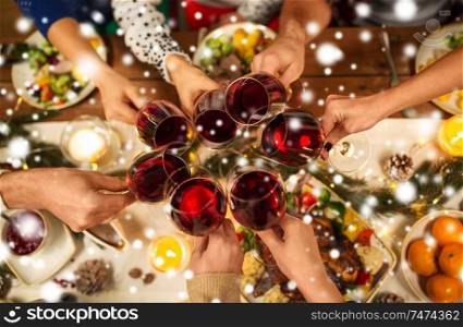 holidays and celebration concept - close up of friends having christmas dinner at home, drinking red wine and clinking glasses over snow. close up of friends with wine celebrate christmas